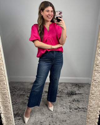 Woman in a pink blouse and blue jeans taking a mirror selfie.
