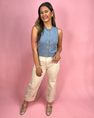 Woman wearing a blue sleeveless top and beige pants against a pink background
