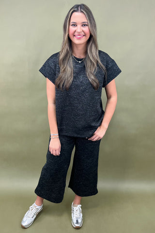Woman wearing a black t-shirt and black pants on a beige background