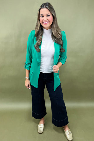 Woman wearing a green blazer, white top, and black pants on a green background