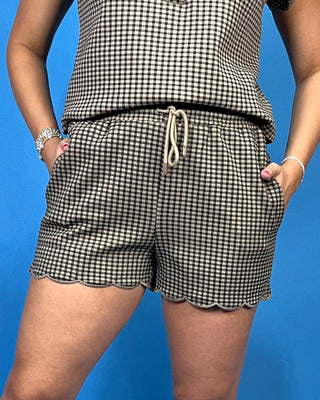 A person wearing black and beige gingham check shorts with a scalloped hem and a matching top