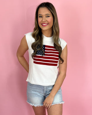 Woman wearing a white sleeveless top with an American flag design on a pink background