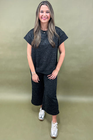 Woman wearing a dark gray outfit with white sneakers on a beige background