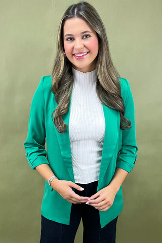 Woman wearing a green blazer over a white sweater on a beige background