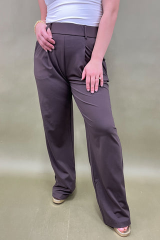 Person wearing brown pants and a white top on a beige background