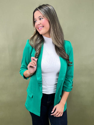 Woman wearing a green blazer over a white sweater on a beige background