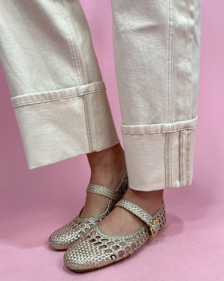 Silver open-toe shoes worn with light-colored pants on a pink background