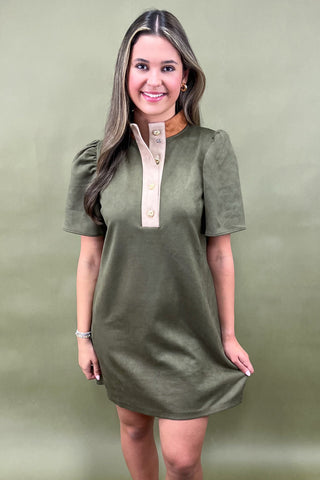 Woman wearing an olive green dress with a beige collar against a green background