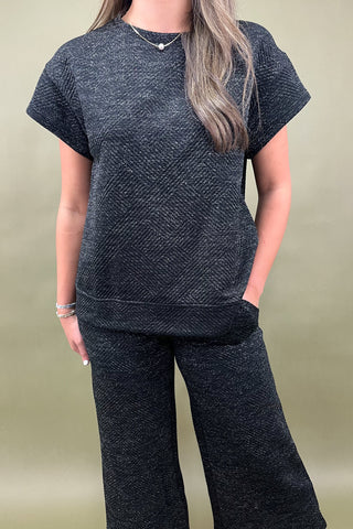 Person wearing a dark gray textured outfit against a plain background