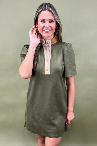 Woman wearing an olive green dress with a beige collar against a green background