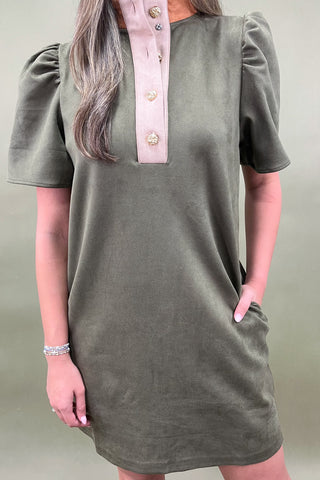 Person wearing a green dress with a pink collar against a neutral background