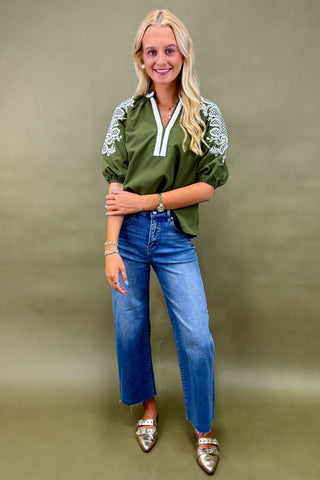 Woman wearing a green embroidered blouse and blue jeans on a beige background