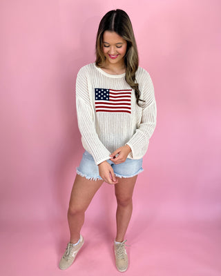 Woman wearing a white sweater with an American flag design on a pink background