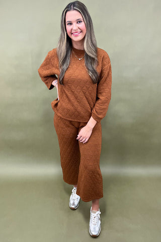 Woman wearing a brown outfit with white sneakers against a beige background
