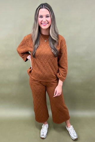 Woman wearing a brown textured sweater and pants set against a plain background