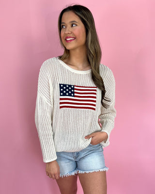 Woman wearing a white sweater with an American flag design against a pink background