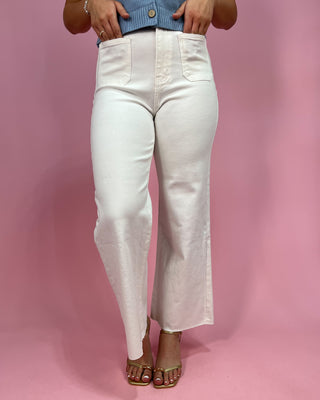 Person wearing white jeans against a pink background