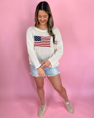 Woman wearing a white sweater with an American flag design on a pink background