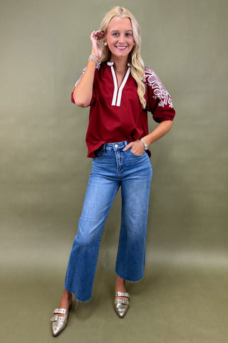 Woman wearing a red top with white accents and blue jeans on a green background
