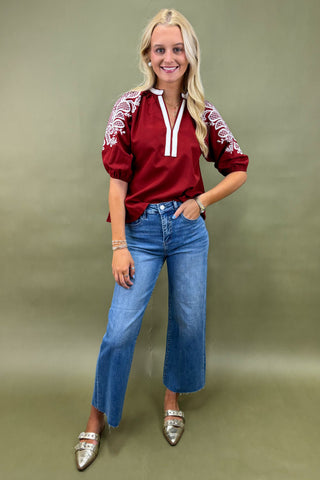 Woman wearing a red embroidered blouse and blue jeans against a green background