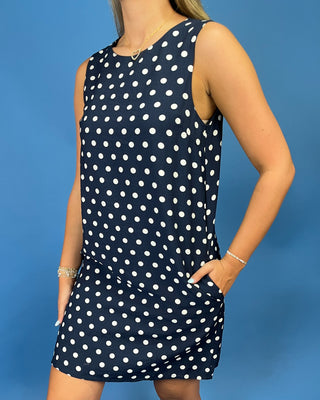 A sleeveless navy blue dress with a white polka dot pattern, worn by a model against a solid blue background.