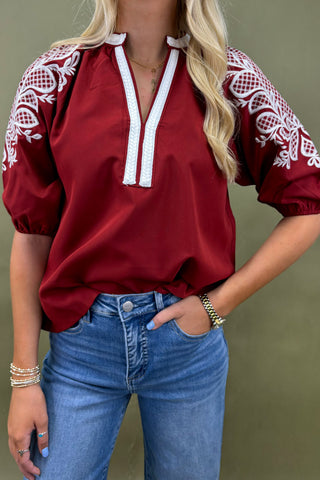 Woman wearing a red blouse with white embroidery and blue jeans against a green background