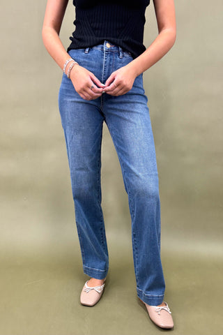 Person wearing blue jeans and a black top on a beige background