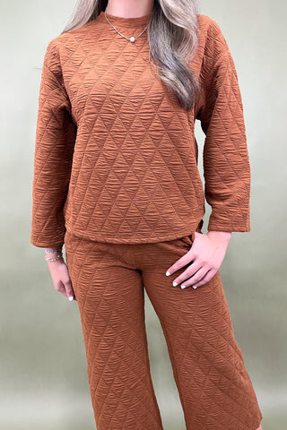 Woman wearing a brown textured sweater and pants set on a plain background