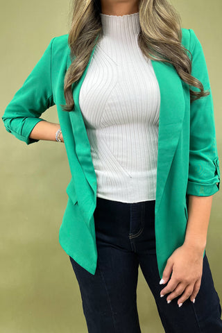 Person wearing a green blazer over a white top and dark jeans on a beige background