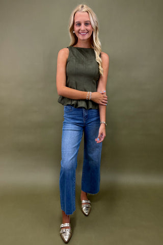 Woman wearing an olive green sleeveless top and blue jeans against a plain background