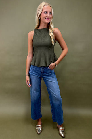 Woman wearing an olive green sleeveless top and blue jeans against a green background