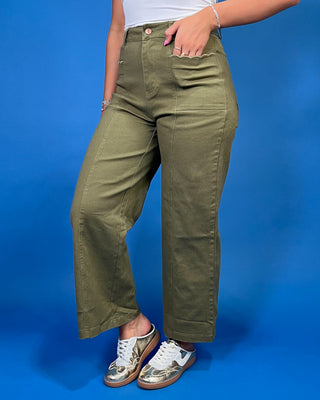 A person wearing olive green wide-leg cropped pants with a white top and metallic sneakers