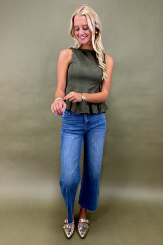 Woman wearing a green sleeveless top and blue jeans against a plain background