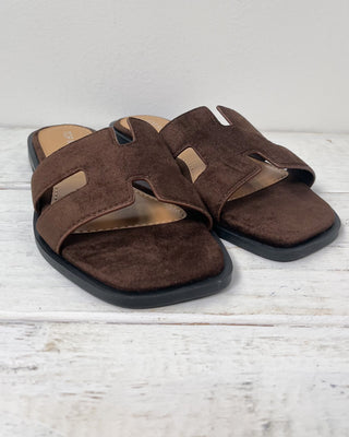 Brown sandal with a hand holding it on a light gray background