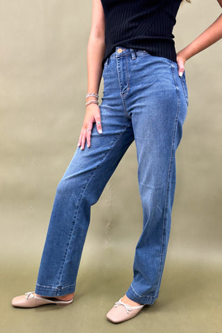 Person wearing blue jeans and a black top on a beige background
