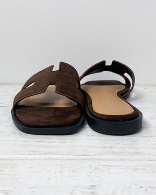 Brown sandal with a hand holding it on a light gray background
