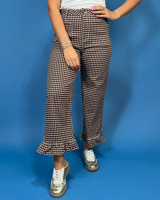 A person wearing high-waisted black and white micro-checkered flare pants with ruffled hems, paired with a white top and metallic silver sneaker