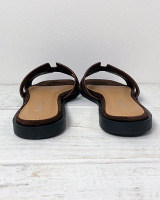 Brown sandal with a hand holding it on a light gray background