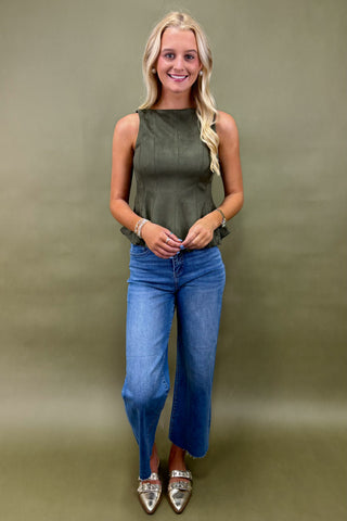 Woman wearing an olive green sleeveless top and blue jeans against a green background