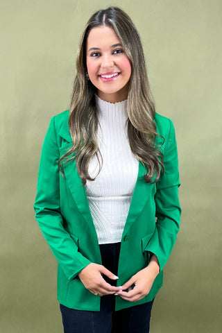 Woman wearing a green blazer over a white sweater on a beige background