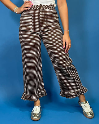 A person wearing high-waisted, wide-leg cropped pants with a brown and white gingham pattern and ruffled hems, paired with white sneakers