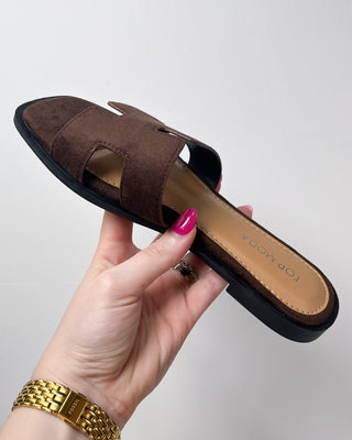 Brown sandal with a hand holding it on a light gray background