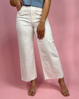 Person wearing white wide-leg pants against a pink background