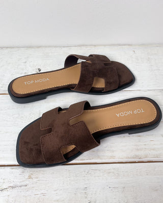 Brown sandal with a hand holding it on a light gray background