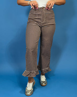 A person wearing brown and white houndstooth flared pants with a ruffled hem, paired with a white top and metallic silver sneakers