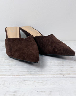 Pair of brown suede mules on a light wooden floor.
