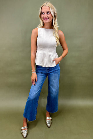 Woman wearing a white sleeveless top and blue jeans against a green background