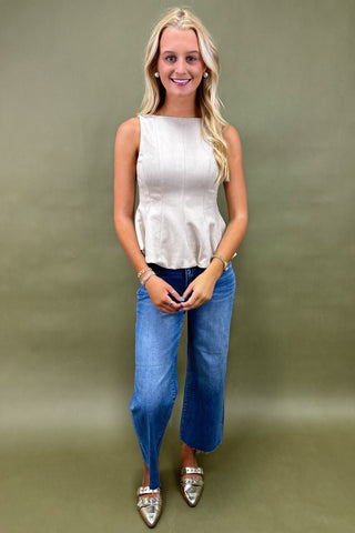 Woman wearing a white sleeveless top and blue jeans against a green background