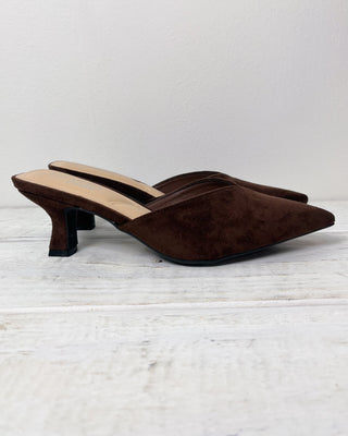 Brown suede shoes with a pointed toe and low heel on a light wooden floor.