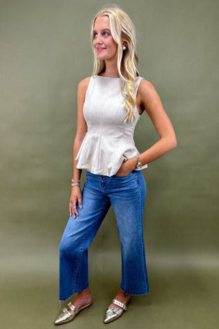 Woman wearing a white sleeveless top and blue jeans against a green background